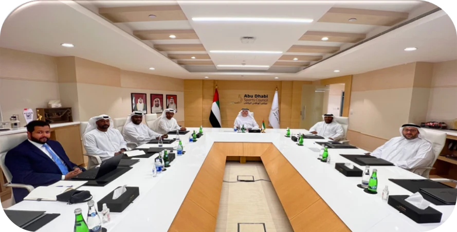 مسؤولون حول طاولة الاجتماعات في مجلس أبوظبي الرياضي، وشعار المجلس وعلم الإمارات خلف المقعد الرئيسي